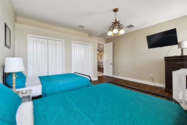 bedroom featuring an inviting chandelier, dark hardwood / wood-style floors, and two closets