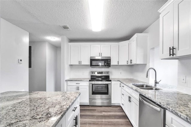 kitchen with appliances with stainless steel finishes, sink, white cabinets, dark wood-type flooring, and light stone counters