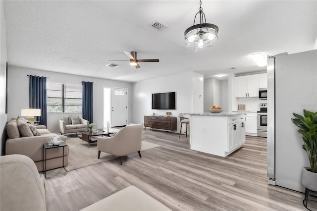 living room featuring a textured ceiling, light wood-type flooring, and ceiling fan