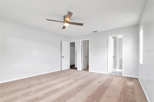 unfurnished bedroom featuring light carpet, ceiling fan, a textured ceiling, and ensuite bath