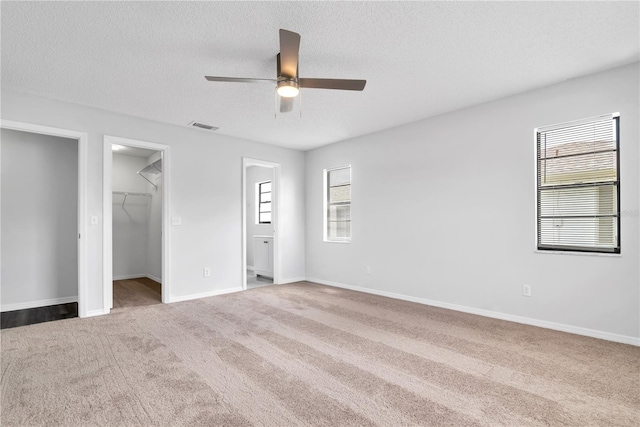 unfurnished bedroom with a textured ceiling, a walk in closet, carpet floors, and ceiling fan