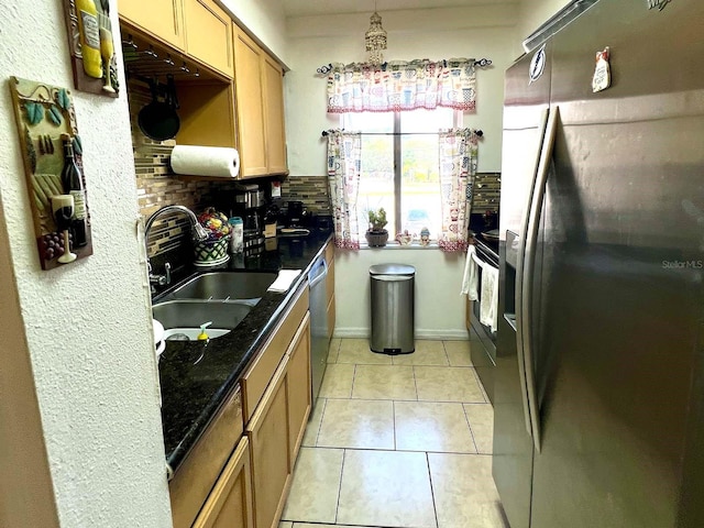 kitchen with appliances with stainless steel finishes, light tile floors, sink, tasteful backsplash, and dark stone countertops