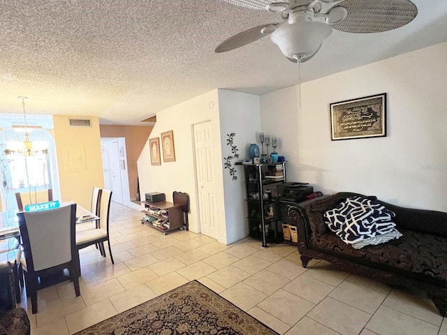 living room featuring ceiling fan with notable chandelier, a textured ceiling, and light tile floors