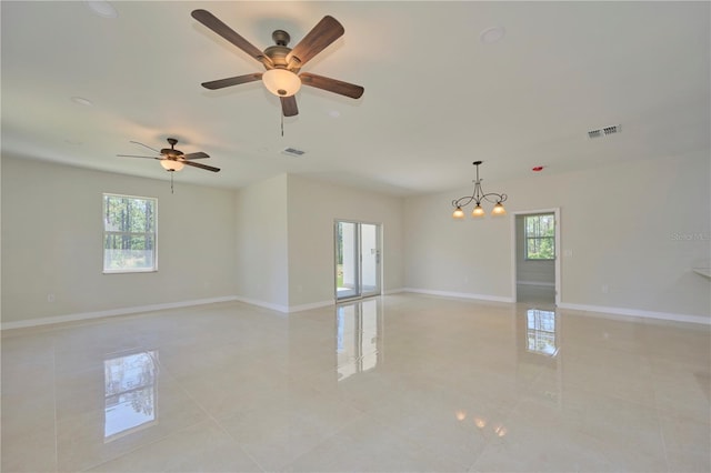 tiled spare room featuring plenty of natural light and ceiling fan with notable chandelier