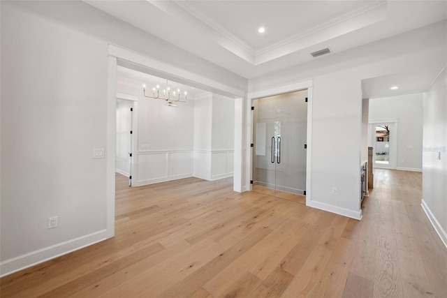 spare room with ornamental molding, light hardwood / wood-style floors, a raised ceiling, and a chandelier