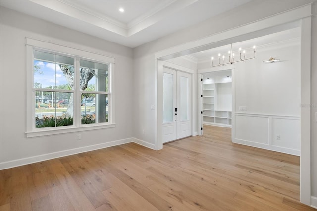 unfurnished room with crown molding, a tray ceiling, a chandelier, and light hardwood / wood-style flooring