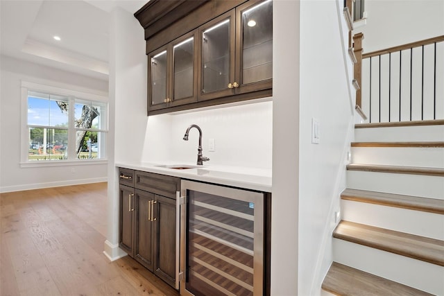 bar featuring sink, dark brown cabinetry, a tray ceiling, light hardwood / wood-style floors, and beverage cooler