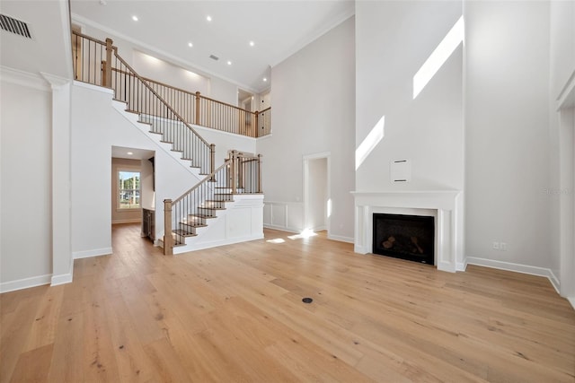 unfurnished living room with ornamental molding, a high ceiling, and light wood-type flooring
