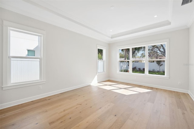 empty room with a raised ceiling, ornamental molding, and light wood-type flooring