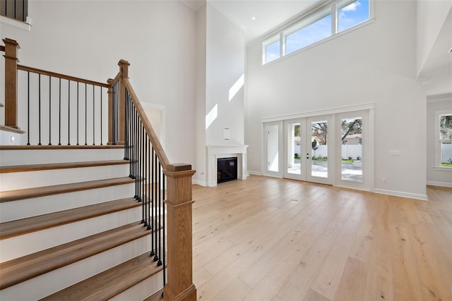 interior space featuring plenty of natural light, a towering ceiling, light hardwood / wood-style floors, and french doors