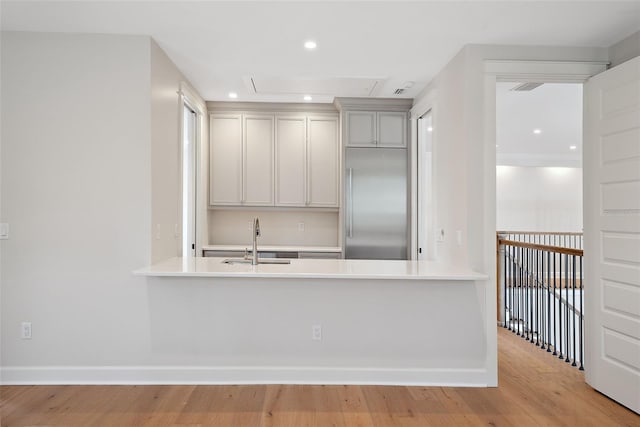 kitchen featuring built in fridge, sink, light hardwood / wood-style floors, and kitchen peninsula