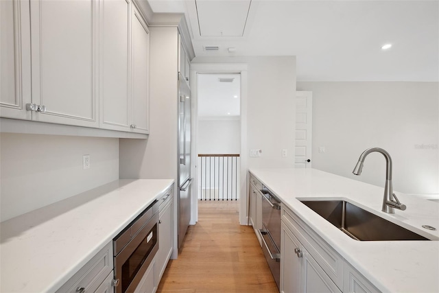 kitchen with sink, light hardwood / wood-style flooring, appliances with stainless steel finishes, white cabinetry, and light stone countertops