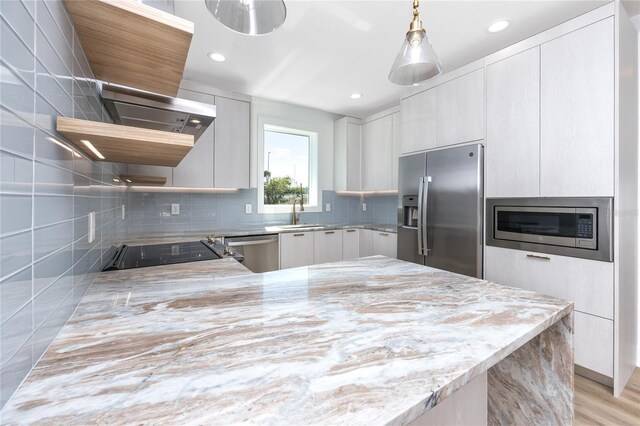 kitchen with kitchen peninsula, appliances with stainless steel finishes, exhaust hood, decorative light fixtures, and light hardwood / wood-style flooring