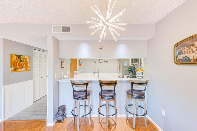 kitchen with kitchen peninsula, light hardwood / wood-style floors, an inviting chandelier, and a kitchen bar