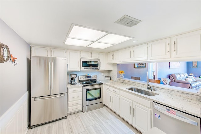 kitchen with white cabinets, appliances with stainless steel finishes, sink, light stone counters, and tasteful backsplash