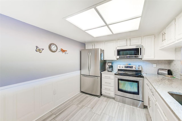 kitchen featuring light stone countertops, stainless steel appliances, tasteful backsplash, white cabinets, and light tile floors