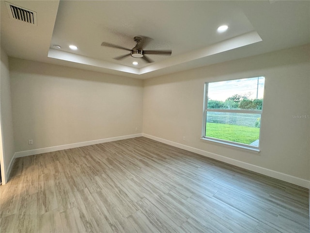 spare room with light wood-type flooring, ceiling fan, and a tray ceiling