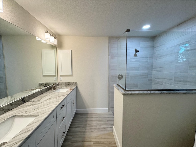 bathroom featuring dual sinks, oversized vanity, tiled shower, wood-type flooring, and a textured ceiling