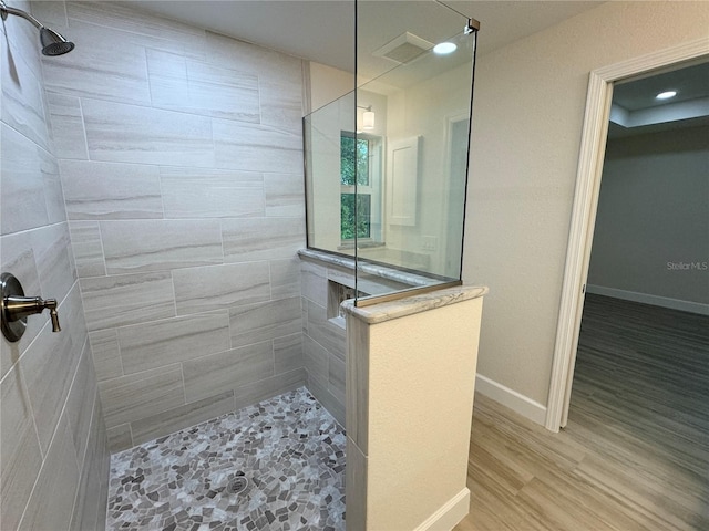 bathroom with a tile shower and wood-type flooring