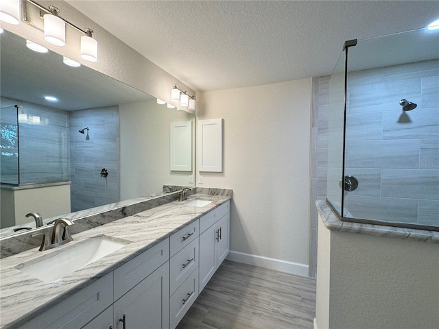 bathroom featuring wood-type flooring, a textured ceiling, dual sinks, tiled shower, and oversized vanity