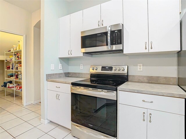 kitchen with appliances with stainless steel finishes, white cabinetry, and light tile floors