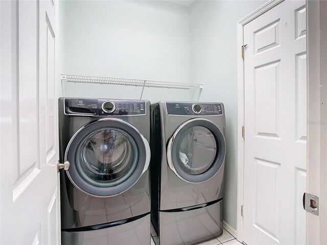 clothes washing area with light tile floors and washer and dryer