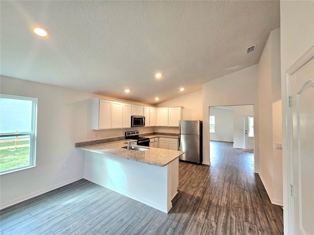 kitchen with kitchen peninsula, appliances with stainless steel finishes, dark hardwood / wood-style floors, a textured ceiling, and white cabinetry