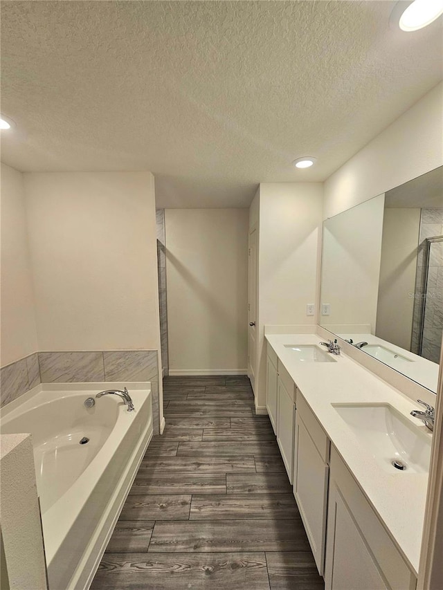 bathroom featuring a washtub, large vanity, a textured ceiling, dual sinks, and hardwood / wood-style flooring