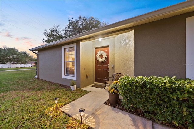 exterior entry at dusk featuring a lawn