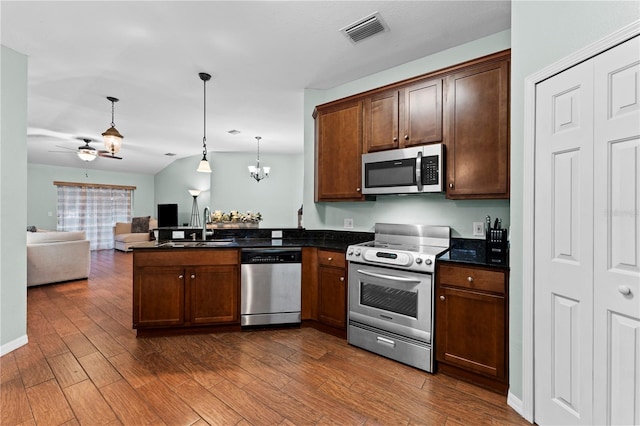 kitchen with ceiling fan with notable chandelier, dark hardwood / wood-style flooring, kitchen peninsula, stainless steel appliances, and sink