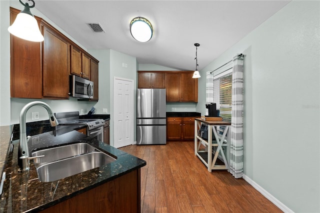 kitchen featuring pendant lighting, appliances with stainless steel finishes, sink, hardwood / wood-style flooring, and dark stone countertops