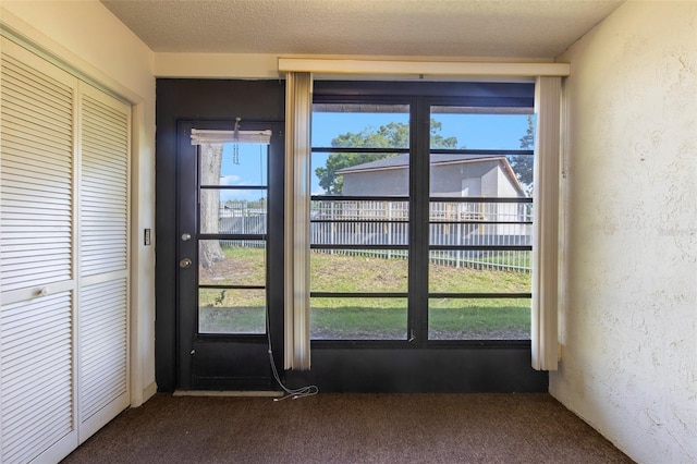 doorway featuring plenty of natural light, dark colored carpet, and a textured ceiling