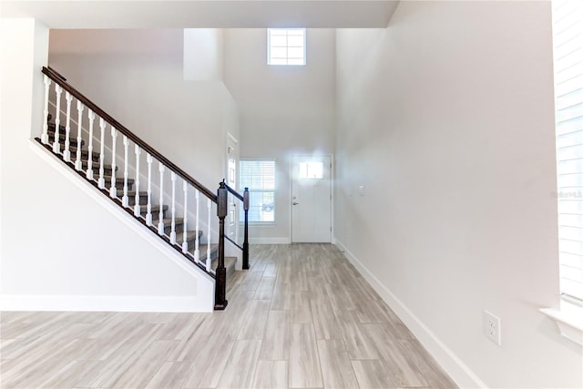 entrance foyer featuring a towering ceiling, a wealth of natural light, and light wood-type flooring