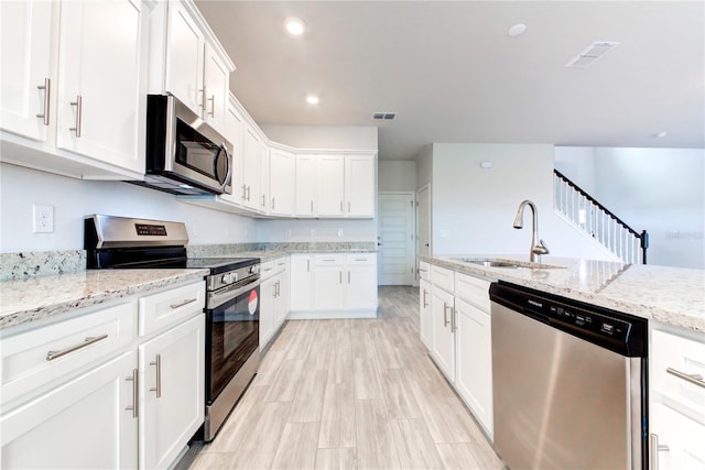 kitchen with appliances with stainless steel finishes, white cabinetry, sink, light stone countertops, and light wood-type flooring