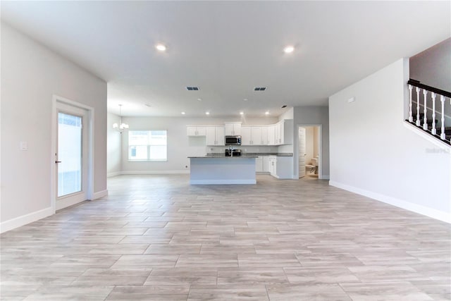 unfurnished living room featuring an inviting chandelier and light hardwood / wood-style floors