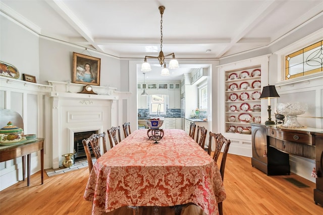 dining space featuring built in features, sink, beam ceiling, coffered ceiling, and light wood-type flooring