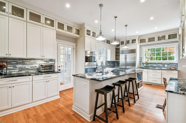 kitchen with a kitchen bar, dark stone countertops, appliances with stainless steel finishes, an island with sink, and white cabinets