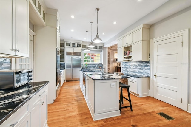 kitchen with hanging light fixtures, a center island with sink, appliances with stainless steel finishes, a kitchen breakfast bar, and dark stone counters