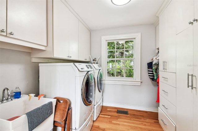 washroom featuring cabinets, sink, washing machine and clothes dryer, and light hardwood / wood-style flooring