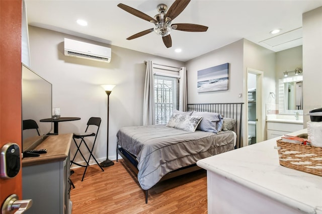 bedroom featuring connected bathroom, a wall mounted air conditioner, light hardwood / wood-style floors, and ceiling fan