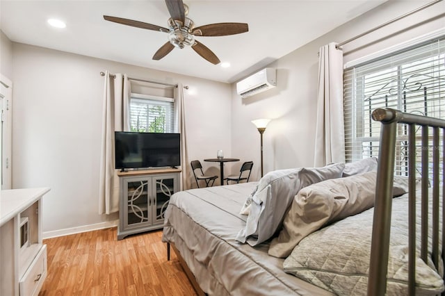 bedroom with ceiling fan, a wall mounted air conditioner, and light hardwood / wood-style floors