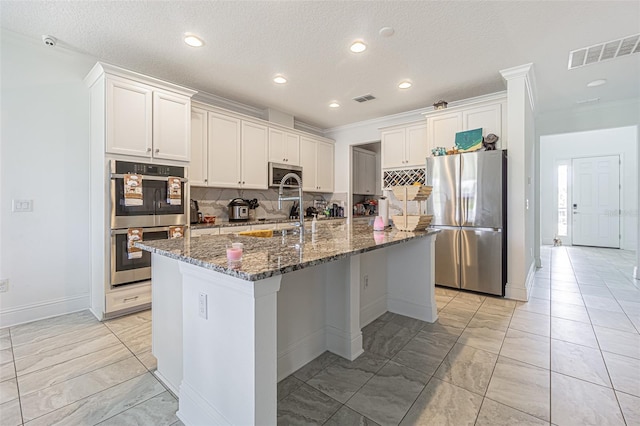 kitchen with white cabinets, dark stone countertops, an island with sink, and appliances with stainless steel finishes