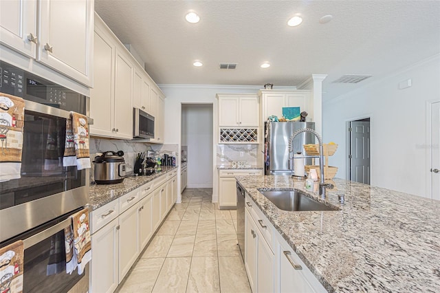 kitchen with light stone countertops, tasteful backsplash, ornamental molding, stainless steel appliances, and white cabinetry