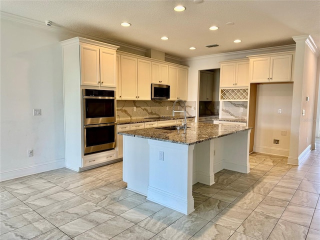 kitchen with dark stone counters, sink, an island with sink, and stainless steel appliances