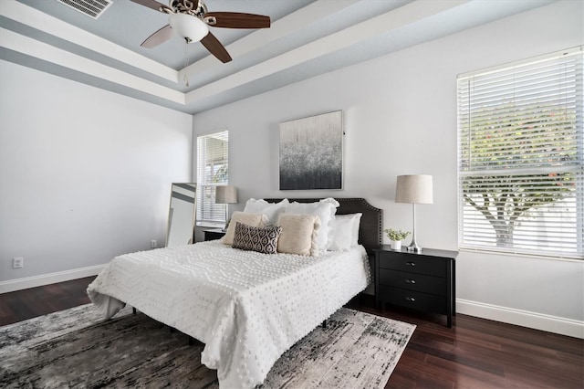 bedroom with dark hardwood / wood-style flooring, ceiling fan, and a tray ceiling