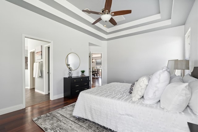 bedroom with ceiling fan, a tray ceiling, and dark hardwood / wood-style floors