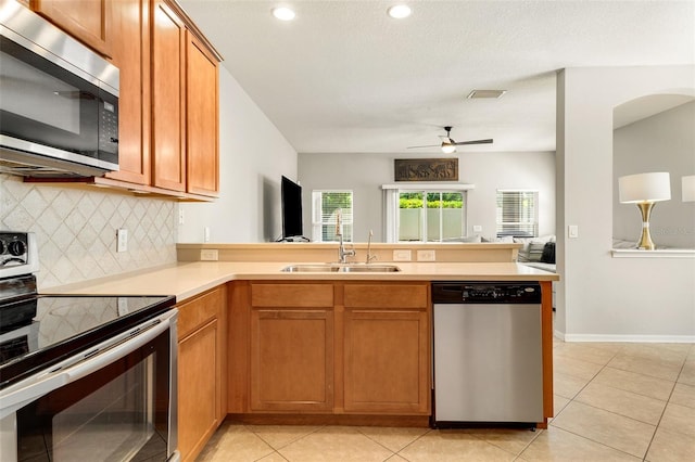 kitchen featuring kitchen peninsula, stainless steel appliances, sink, tasteful backsplash, and ceiling fan