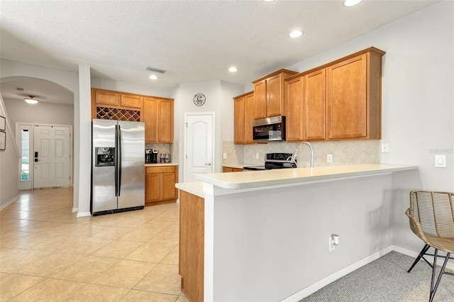 kitchen featuring backsplash, kitchen peninsula, appliances with stainless steel finishes, and light tile floors