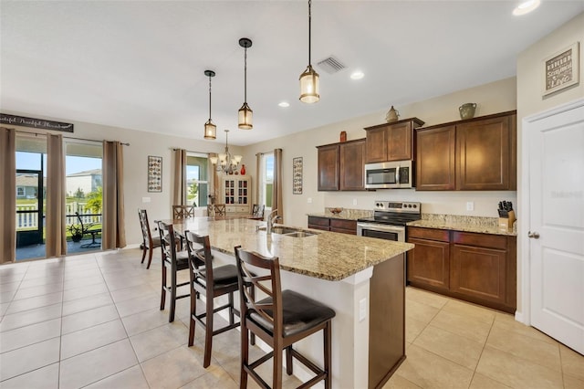 kitchen with a kitchen bar, stainless steel appliances, an island with sink, light stone counters, and pendant lighting