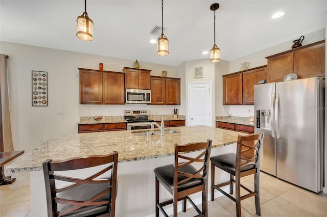 kitchen with appliances with stainless steel finishes, light tile floors, a breakfast bar, decorative light fixtures, and a center island with sink